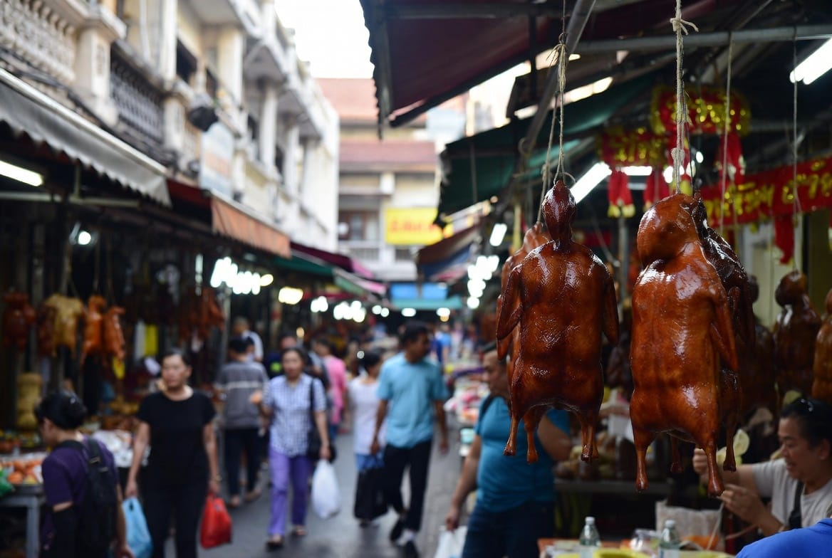 Roast ducks hanging in glass cases along Yaowarat Road at night